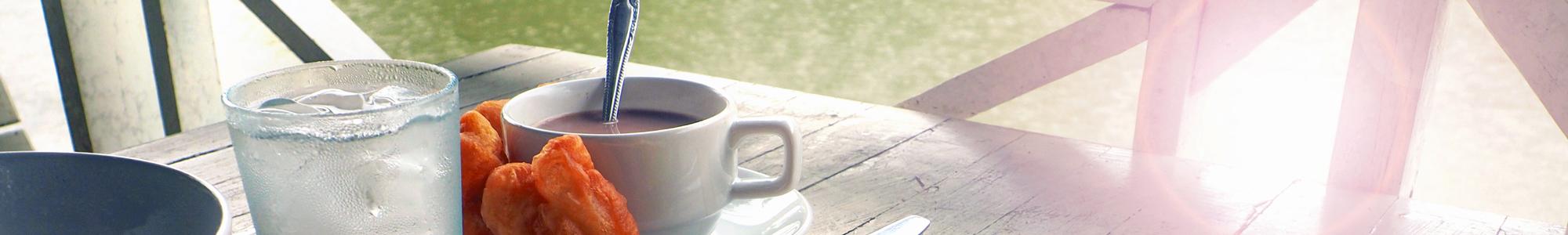 Bannerbillede med en kop kaffe og et glas vand på et havebord i solskin