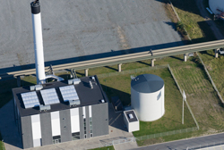 Luftfoto af varmeværket. En sort firkantet bygning med en høj hvid skorsten.
